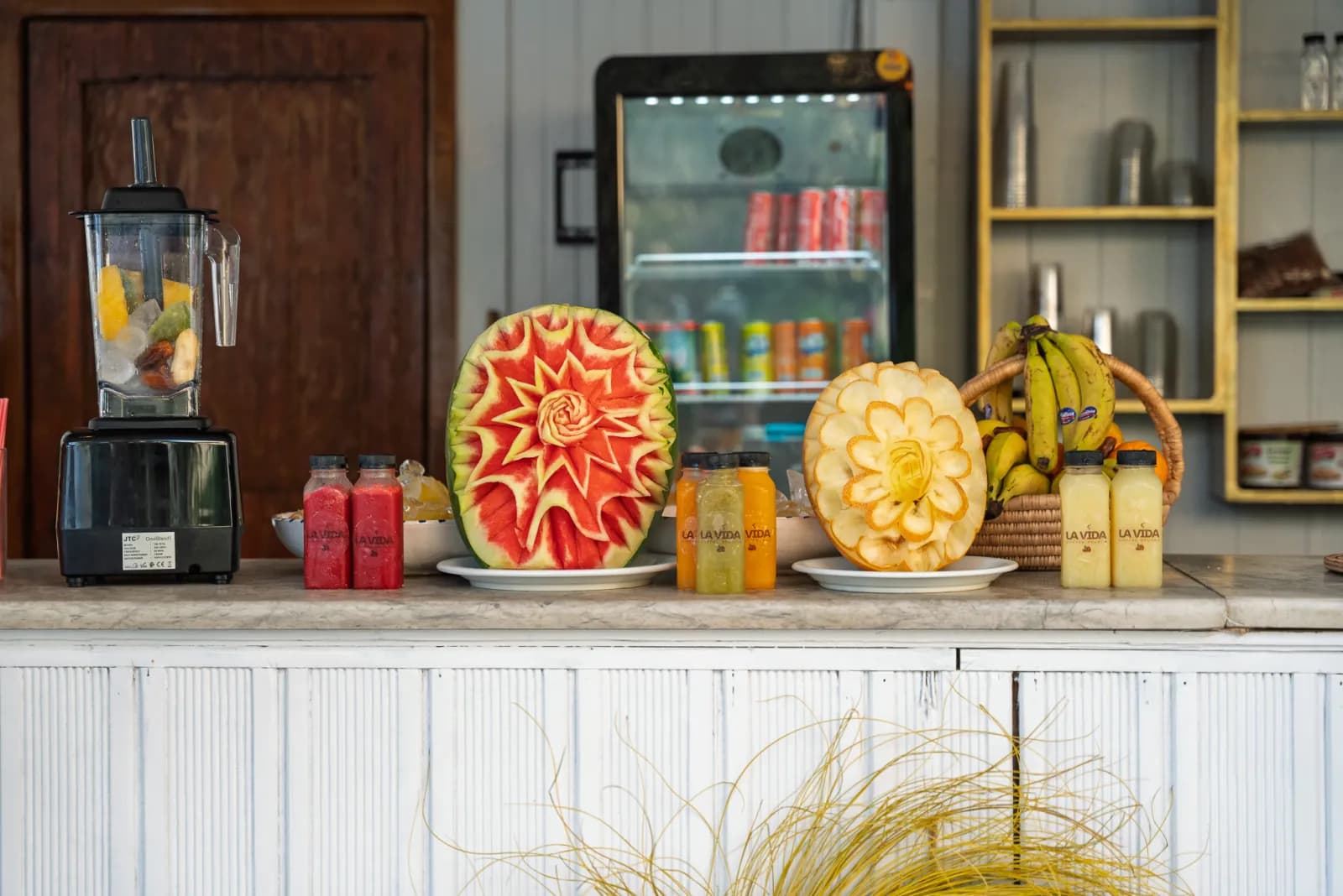 Le comptoir à jus du café : pastèque et melon sculptés, jus pressés du jour et corbeille de fruits