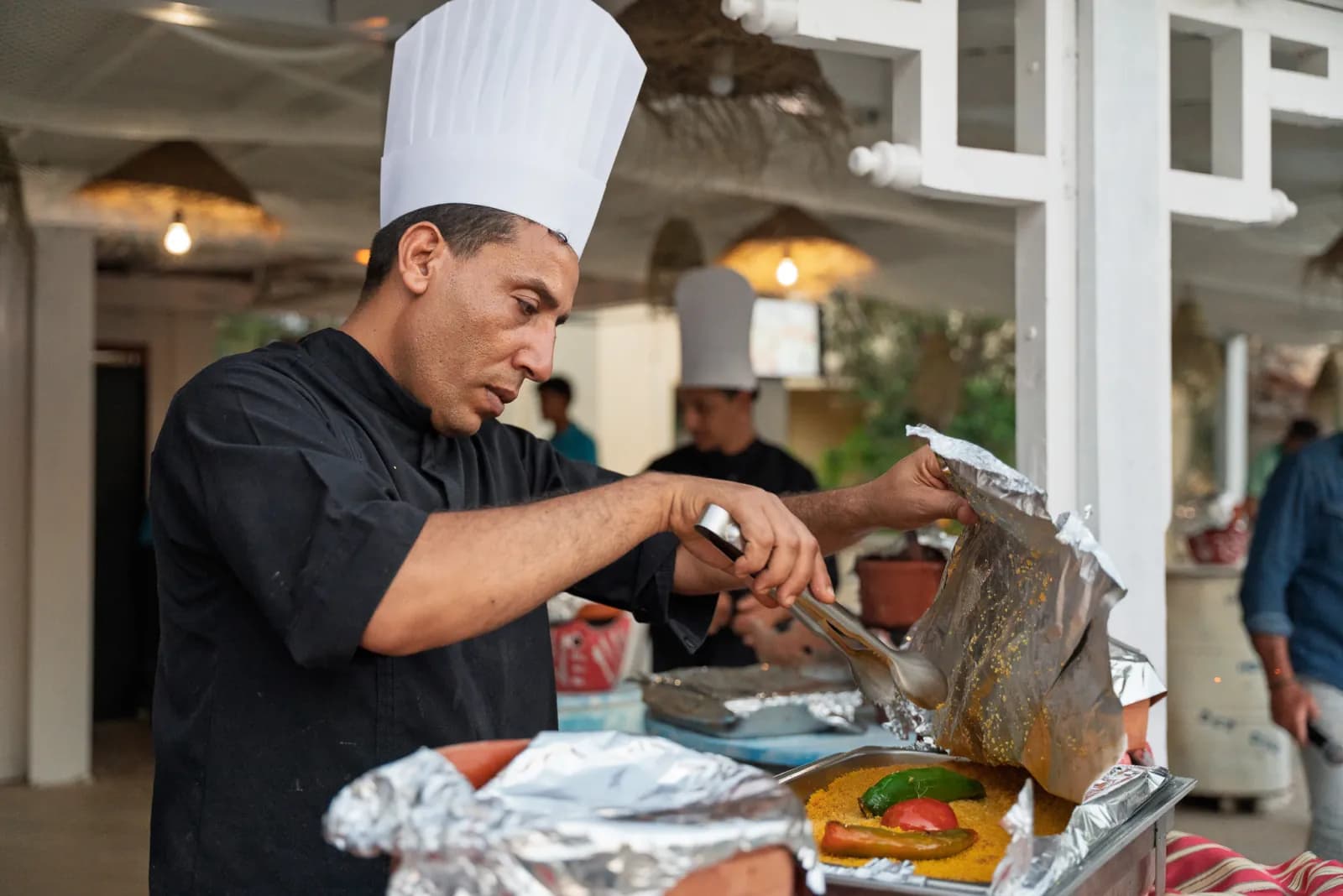 Le chef sert le couscous au poivron et à la tomate, sous la pergola du restaurant
