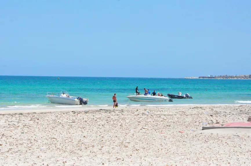 La plage : sable clair, eau turquoise et les bateaux des activités nautiques au bord