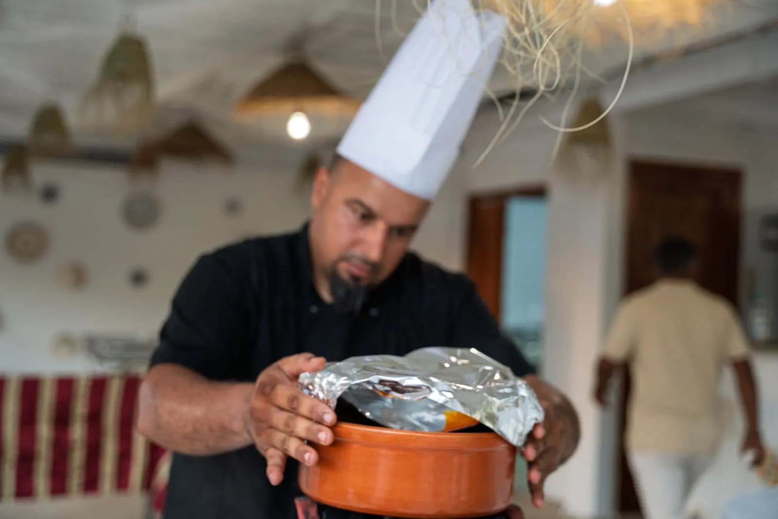 Le chef ouvre un plat en terre cuite sous la pergola